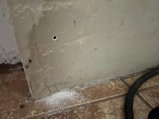 A wall with a small hole and scattered white powder on the floor.